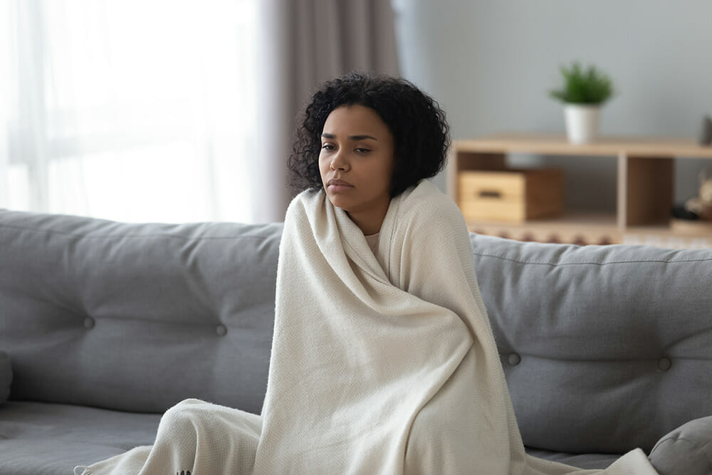 Sick african woman feeling cold covered with blanket at home